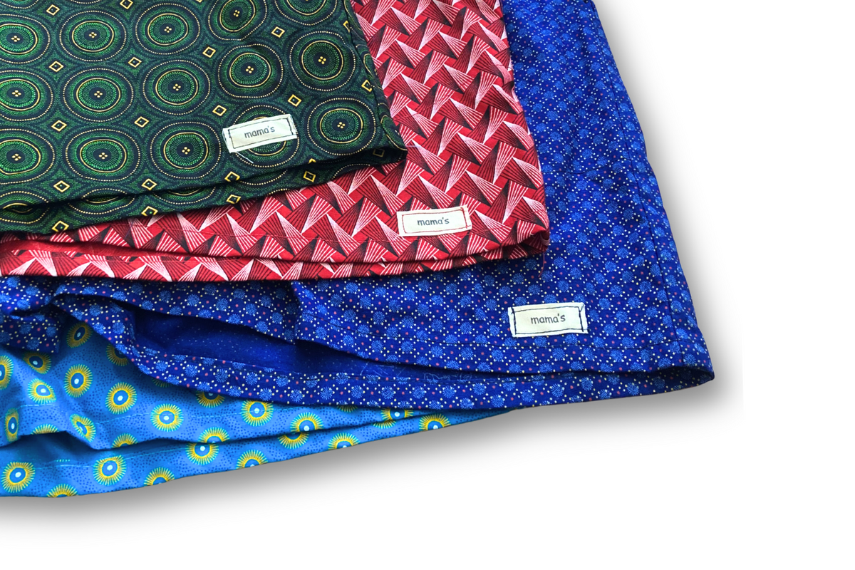 Four folded patterned fabric pieces stacked diagonally on a white background, each with a small white label reading 'Pinnock'. The fabrics show different prints: dark green with circular motifs, red and pink with zigzag patterns, bright blue with small dots, and light blue with yellow circular motifs.